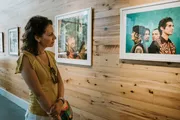 A woman is observing framed photographs displayed in an art gallery with wooden walls.