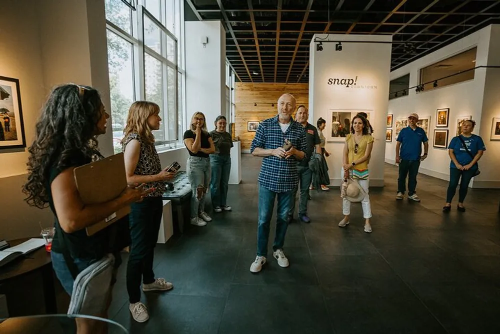 A group of people is attentively listening to a speaker in a gallery with photographic artwork displayed on the walls