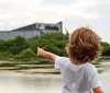 A child with curly hair is pointing towards the Space Shuttle exhibit at the Kennedy Space Center as seen across a body of water