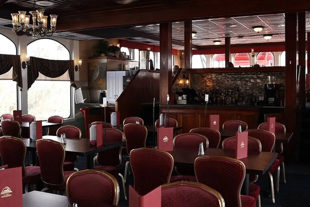 The image depicts an empty restaurant interior with red and cream chairs set tables and a bar area in the background exuding a classic and welcoming atmosphere