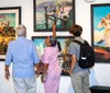 Three individuals are attentively viewing a collection of vibrant paintings at an art gallery