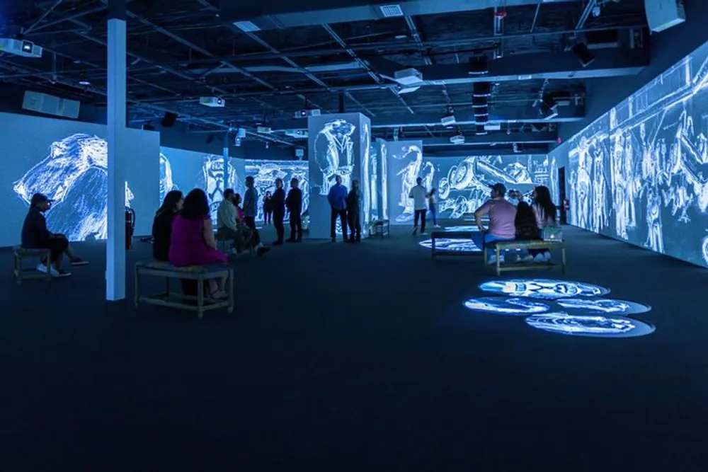 Visitors are experiencing an immersive art installation with large-scale projected visuals on the walls and floor of a dark room