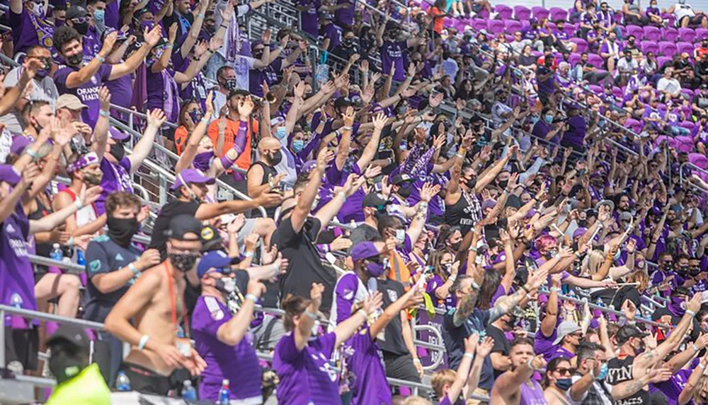 A vibrant crowd of sports fans clad mostly in purple are cheering enthusiastically in a stadium setting