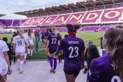 Soccer players are walking onto a stadium with purple seating and the word 