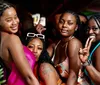 Four women are posing happily for the camera at a social gathering with two of them making peace sign gestures