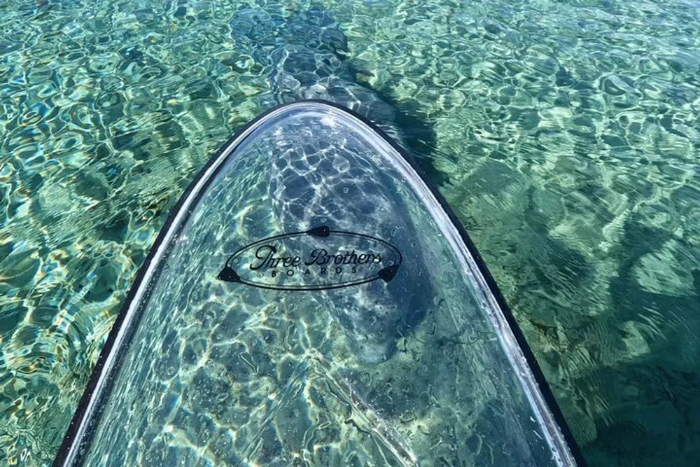 A clear stand-up paddleboard floats on a crystal-clear turquoise water surface