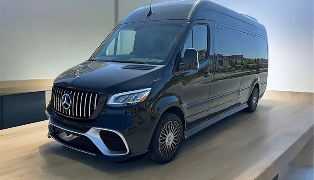 This image shows a luxury van parked indoors featuring a sleek dark blue exterior with a prominent grille and badge indicative of a high-end car manufacturer