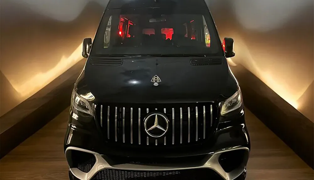 A black Mercedes-Benz van is parked indoors illuminated by soft lighting that highlights its luxury front grille design