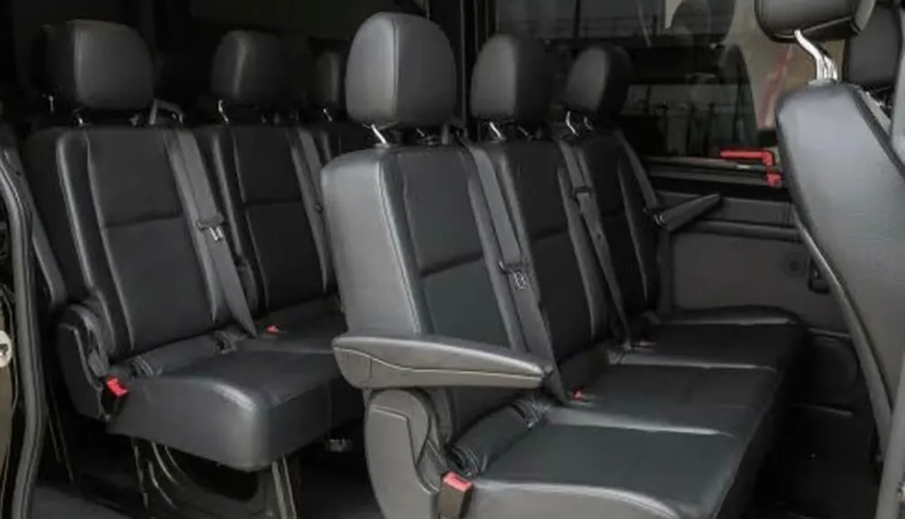 The image shows the interior of a vehicle featuring two rows of clean black leather seats with headrests and seat belts