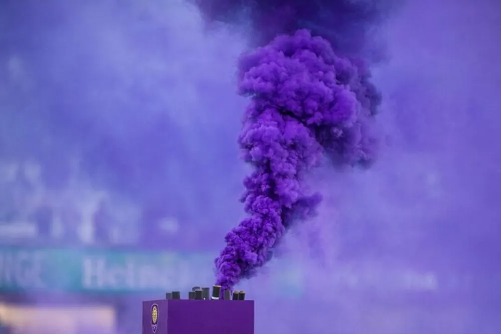 A thick plume of purple smoke is rising from a source obscured by the colorful haze