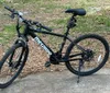 A black mountain bike is parked outdoors on a concrete slab surrounded by grass and leaf litter