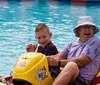 A woman and a young boy are giving thumbs-up signs while seated with safety harnesses in go-karts appearing excited and ready to race