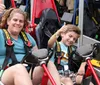 A woman and a young boy are giving thumbs-up signs while seated with safety harnesses in go-karts appearing excited and ready to race