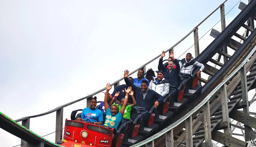 A group of excited riders with raised hands are enjoying a ride on a wooden roller coaster