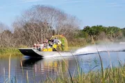 A group of people is enjoying a ride on an airboat through a waterway surrounded by vegetation.