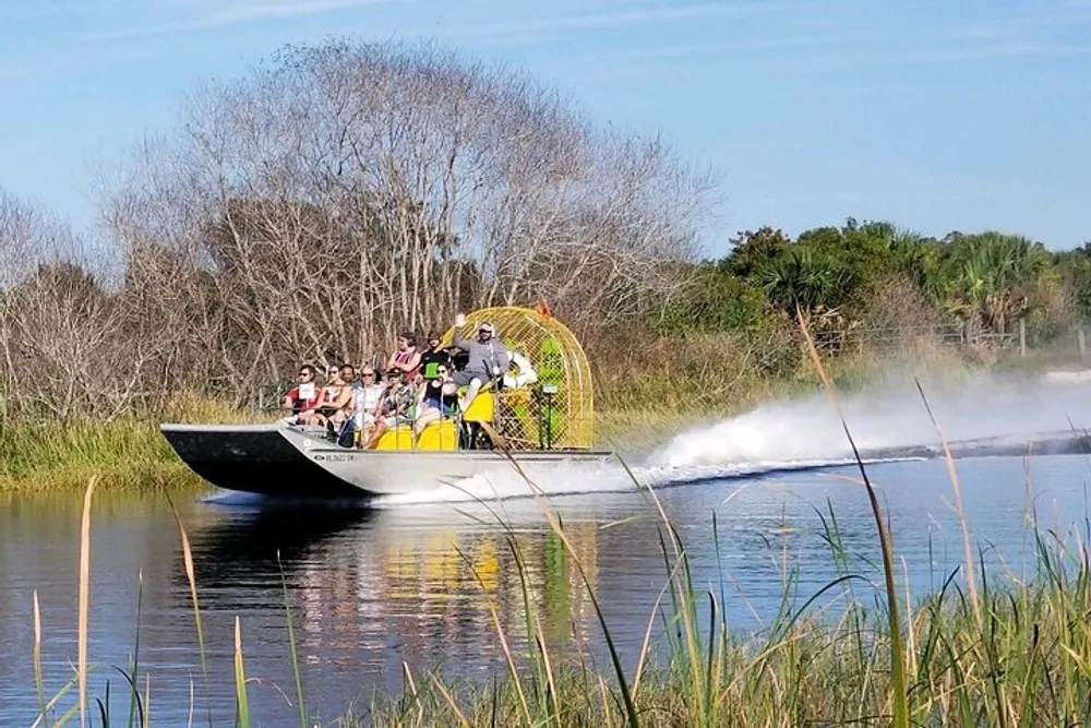 A group of people is enjoying a ride on an airboat through a waterway surrounded by vegetation