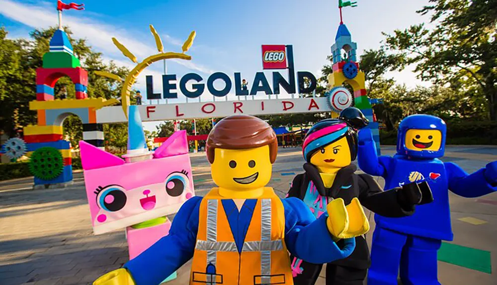 This image features costumed characters resembling LEGO figures in front of the LEGOLAND Florida entrance with colorful LEGO sculptures and the parks sign in the background