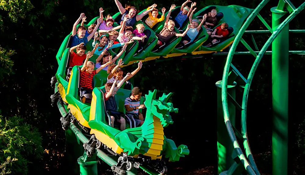 A group of excited people are raising their arms while riding a dragon-themed roller coaster amidst green foliage