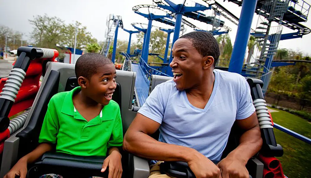 A young boy and a man share a fun moment together on a roller coaster with big smiles and excitement on their faces