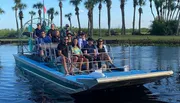 A group of people is enjoying a scenic ride on an airboat in a waterway lined with palm trees.