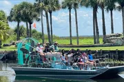 A group of people is enjoying a ride on an airboat among palm trees, likely on a guided tour in a wetland area.