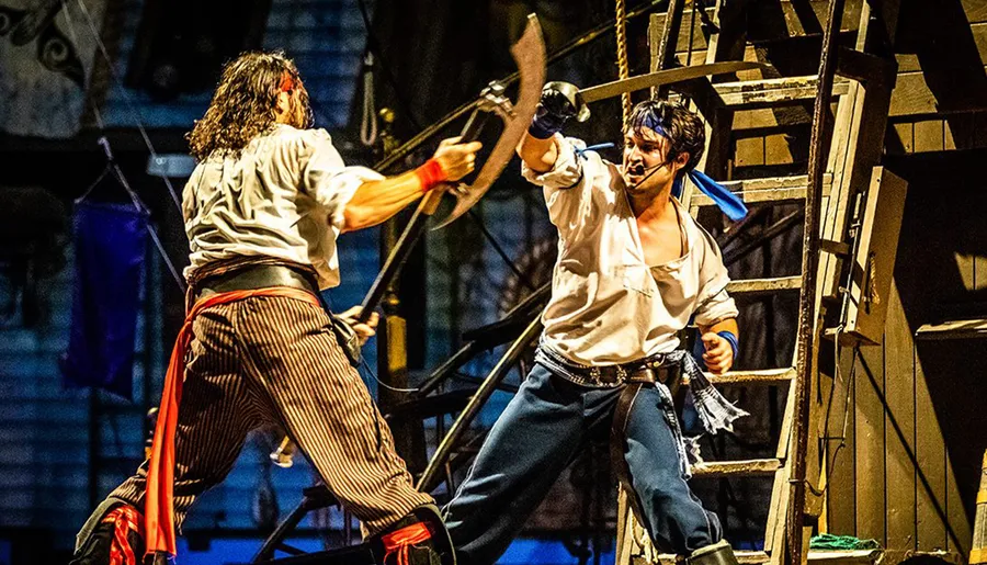 Two actors engaged in a theatrical swashbuckling sword fight on a stage designed to look like a ship's deck.