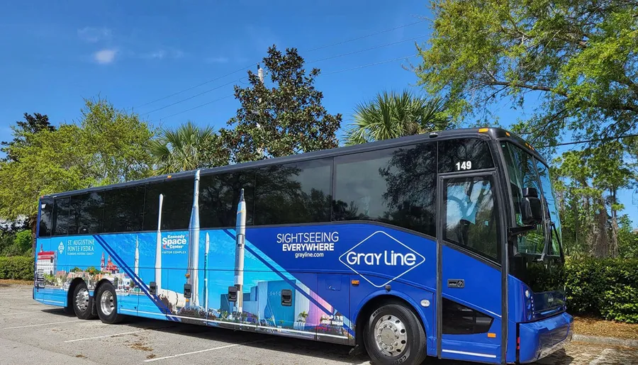 A blue tour bus with advertising wraps is parked under a clear sky with trees in the background.