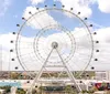 The image showcases a vibrant sunset skyline with a large observation wheel promotional insets for SEA LIFE Orlando Aquarium and Madame Tussauds and people enjoying attractions