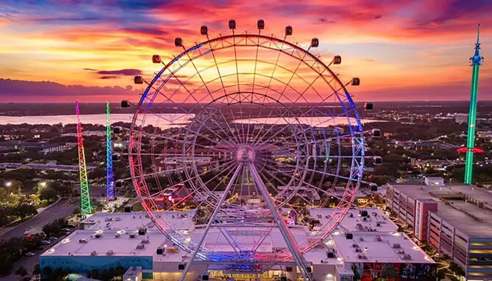 This image captures a vibrant sunset sky backdrop behind a lit-up observation wheel alongside colorful towers suggesting a festive atmosphere in an urban entertainment district