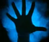 A silhouetted hand is displayed against a blurred blue background creating a mysterious and eerie atmosphere
