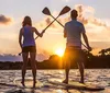 Two people are stand-up paddleboarding on calm water against a beautiful backdrop of a setting sun