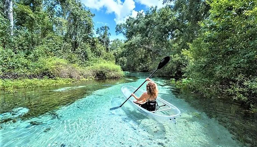 A person is kayaking in a clear blue waterway surrounded by lush greenery.