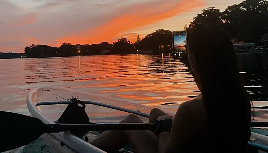 A person is kayaking on calm waters with a stunning sunset in the background.