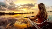 A person is kayaking on calm water during a vibrant sunset.