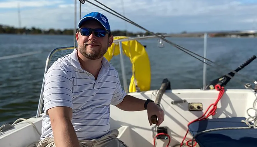 A smiling person is steering a sailboat on a sunny day.