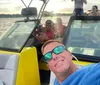 A group of people is enjoying a boat ride on a sunny day with some sitting at the back and one person taking a selfie in the foreground