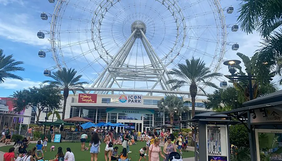 Visitors are enjoying a sunny day at a lively entertainment complex with a large Ferris wheel dominating the skyline.