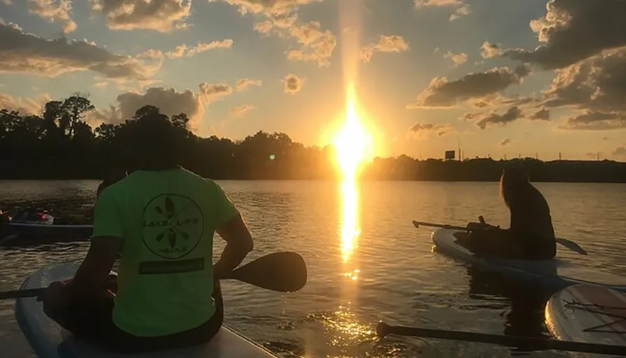 Two individuals are kayaking on calm waters against the backdrop of a stunning sunset.