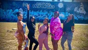 Four women pose confidently in front of a vibrant graffiti wall marked 