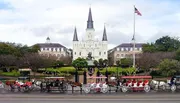 Horse-drawn carriages line up in front of an iconic cathedral surrounded by manicured gardens, under an overcast sky.