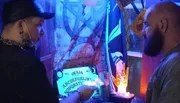 Two people are standing in front of a table with a Ouija board and mystical-themed decorations.