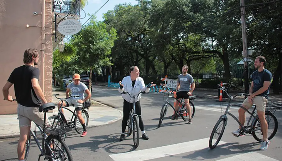 A group of people on bicycles is gathered at an intersection, engaging in conversation in what looks like a leisurely setting with trees and city signs in the background.