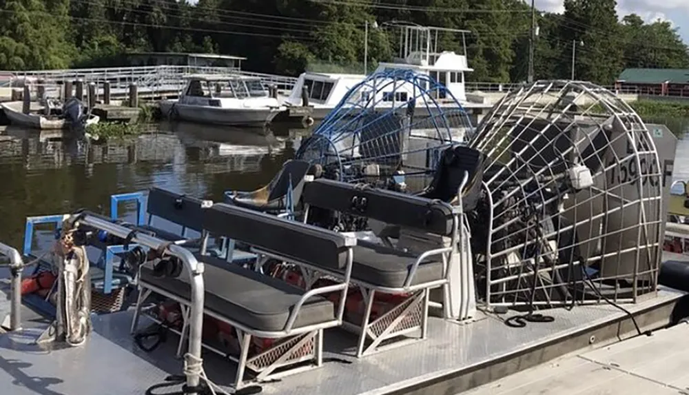 A large airboat is docked at a marina with other boats visible in the background