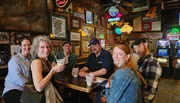 A group of cheerful people are enjoying drinks together at a bar adorned with neon signs and memorabilia on the walls.