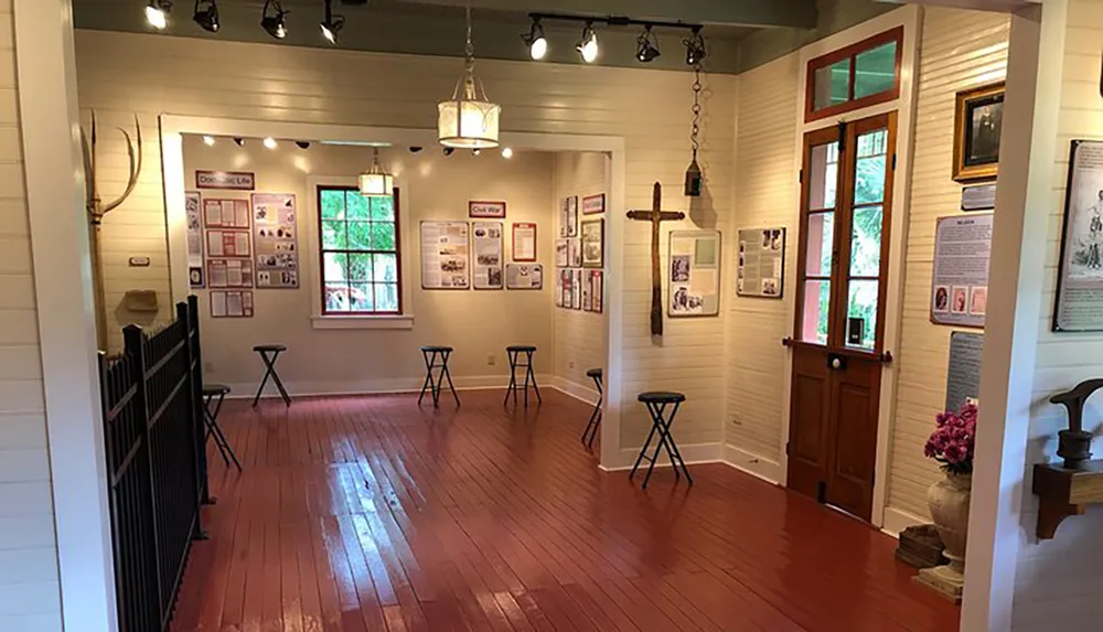 The image depicts an interior view of a gallery or museum with informational wall displays wooden stools and a warm wooden floor