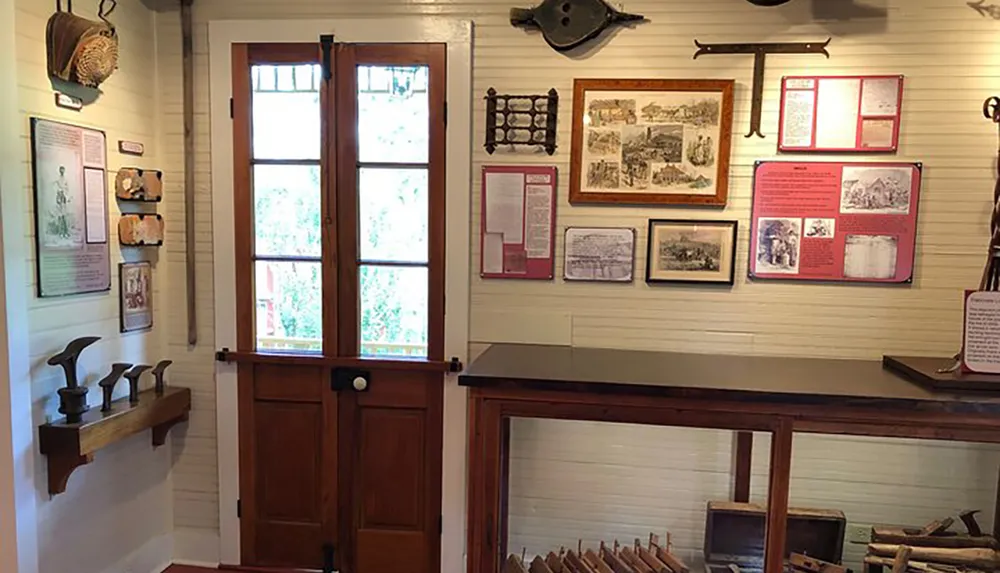 The image shows an interior room likely in a museum with various historical artifacts displayed including tools and framed information on the walls