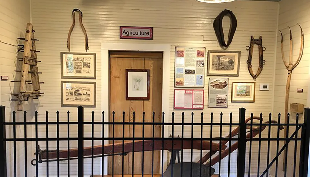 The image shows an interior space set up with agricultural artifacts and informative displays framed by a black metal fence