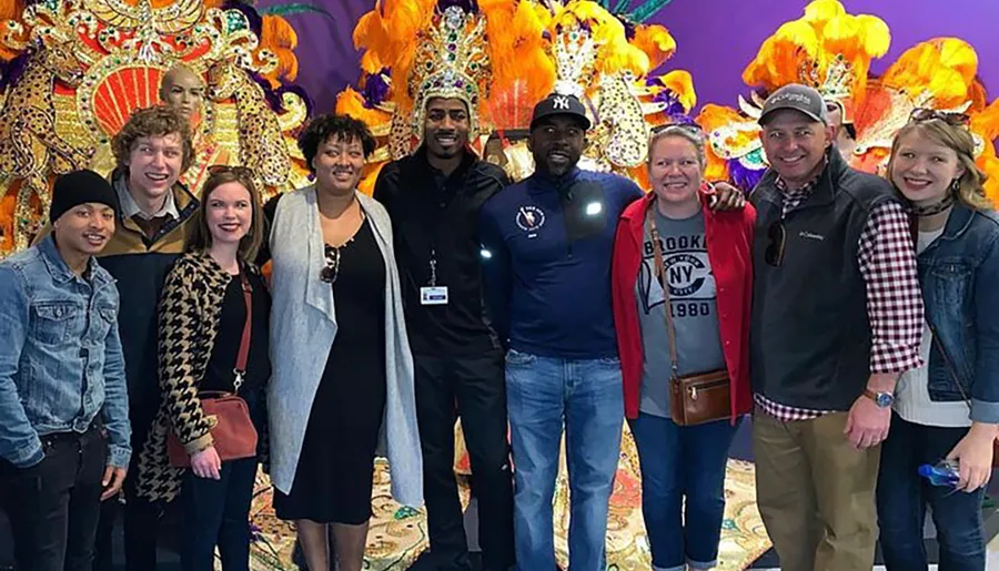 A group of eight smiling people are posing for a photo in front of a colorful feathered backdrop.