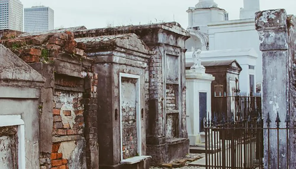 The image shows aged and weathered above-ground tombs in a historic cemetery giving an air of neglect and history amidst a backdrop of modern buildings