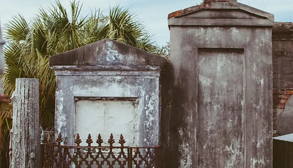 The image shows aged and weathered above-ground tombs featuring crosses and ornamental iron fencing likely in an old cemetery